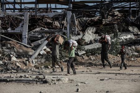 ２１日、イスラエル軍が攻勢をかけるガザ中部で、配給物資を運ぶ人たち（ゲッティ＝共同）