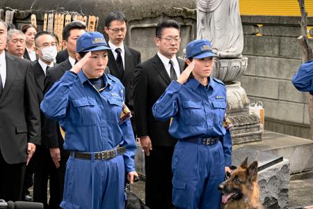 慰霊碑の前で敬礼する警察犬の担当者＝２３日午前、東京都板橋区