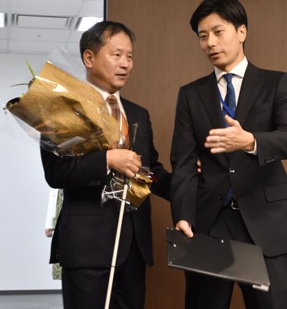 職員（右）の介助を受けながら初登庁した、パラ選手から初のスポーツ庁長官となった河合純一氏＝１日午前、東京・霞が関