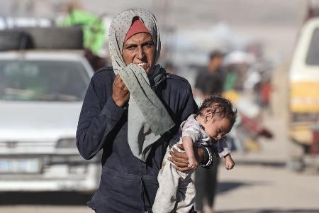 １日、イスラエルの攻撃が激化し、赤ちゃんを抱えて逃げるパレスチナ人の女性＝ガザ北部ガザ市（ゲッティ＝共同）