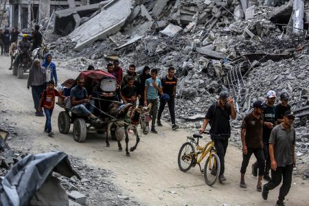 停戦合意発効を受け、自宅に戻るため破壊された建物の間を移動するパレスチナ人ら=12日、ガザ南部ハンユニス(ゲッティ=共同)