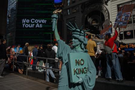 18日、自由の女神像に扮し米ニューヨークで「NO KINGS(王はいらない)」に参加した人(AP=共同)