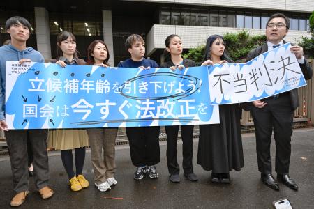 東京地裁による被選挙権年齢引き下げ訴訟判決を受け「不当判決」などと書かれた紙を掲げる原告団=24日午後、東京・霞が関