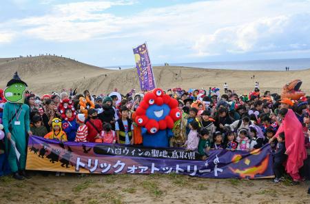 鳥取砂丘で開かれたハロウィーンパーティーに登場した「ミャクミャク」と記念撮影する参加者＝２６日午後、鳥取市