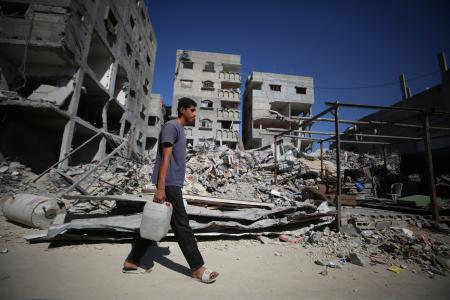 ２６日、ガザのブレイジ難民キャンプで、がれきの前を歩く住民（ゲッティ＝共同）