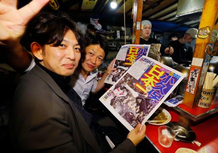 ソフトバンクの日本一を伝える号外を手に、福岡・天神の屋台で喜ぶ客=30日夜