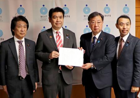 自民党の「大学病院を支援する議員連盟」の松野博一会長（中央右）から緊急決議を受け取る松本文科相＝１１日午後、文科省