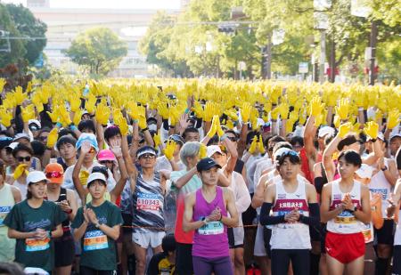 神戸マラソンのスタート前、復興の象徴のヒマワリを表した黄色の手袋を掲げるランナー＝１６日午前、神戸市中央区