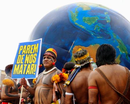 熱帯林保護などを訴え、「私たちを殺すのをやめろ」と書かれたプラカードを掲げる先住民男性＝１５日、ブラジル・ベレン（共同）