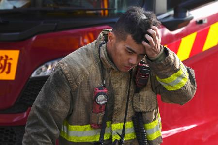 　消火活動が続く高層住宅の火災現場で頭に手をやる消防士＝２８日、香港北部・新界地区大埔（共同）