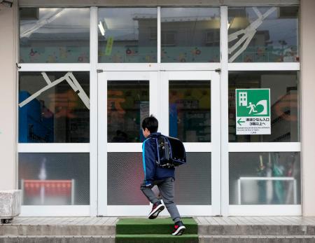 学校が再開し、登校する青森県八戸市立江南小の児童。地震でガラス扉がひび割れた=10日午前7時47分