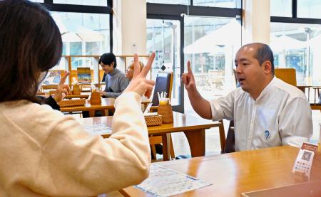 山梨県立美術館のレストラン「ＣＯＬＥＲＥ（コレル）」で、客に手話を教える大久保洋文さん＝１１月、甲府市