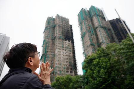 香港の大規模火災から１カ月を迎え、現場の高層住宅群に向かって手を合わせる男性＝２６日（共同）