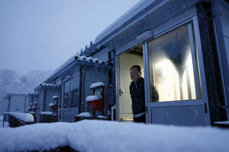 　能登半島地震の発生から２年、仮設住宅で降り積もる雪を見つめる男性＝１日午前７時２分、石川県珠洲市三崎町