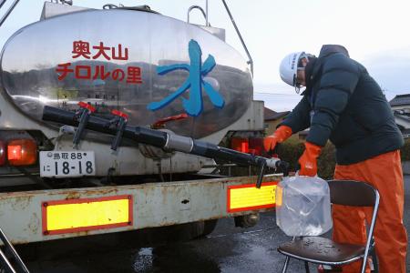 断水が起きている鳥取県南部町で、給水車から水をくむ町職員＝７日午前７時２１分