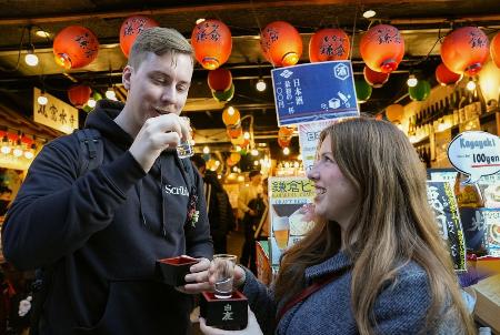 神奈川県鎌倉市の商店街で日本酒を楽しむスウェーデンからの訪日客＝２５年１２月