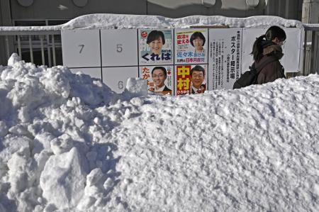 雪の中に立つ衆院選のポスター掲示板。手前の道路には人の背丈ほどの高さに雪が積み上げられていた＝８日午前、北海道小樽市