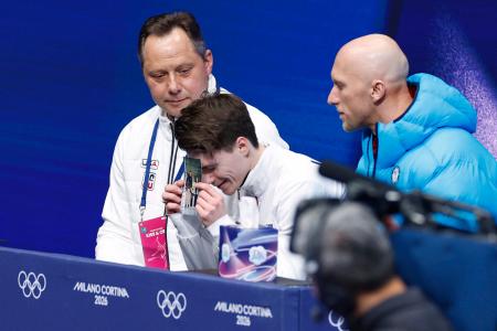 男子ＳＰの得点を確認し、亡き両親の写真に額をつけるマキシム・ナウモフ＝ミラノ（共同）