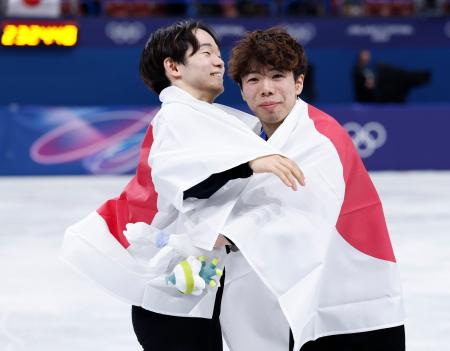 　日の丸をまとって抱き合う、男子で銀メダルの鍵山優真（左）と銅メダルの佐藤駿＝ミラノ（共同）