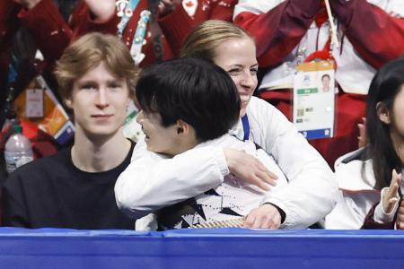 団体男子ＳＰの演技を終え、鍵山優真を抱きしめるカロリナ・コストナー・コーチ（奥）＝７日、ミラノ（共同）