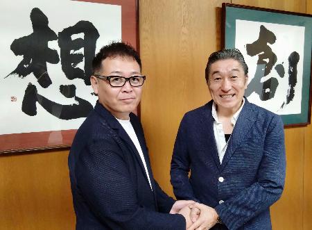 学校法人「国際志学園」の水嶋章陽理事長(右)と握手する「MMA甲子園」を主催する岩崎ヒロユキ代表=2025年7月、北九州市