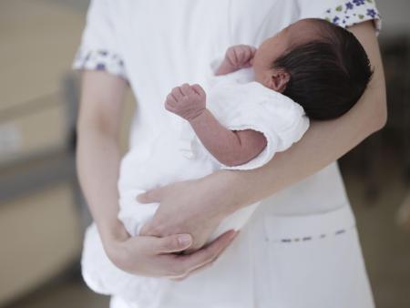 病院で助産師に抱かれる新生児