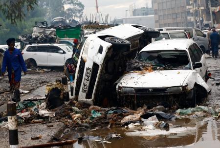 　７日、ケニア・ナイロビで、豪雨の影響で大破した車両の近くを歩く女性（ロイター＝共同）