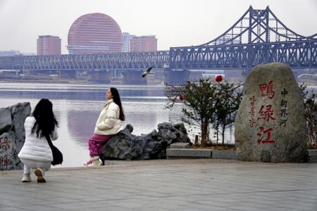 中国遼寧省丹東で北朝鮮側を背景に記念撮影をする女性たち。中朝を結ぶ鉄道橋も見える＝１日（共同）
