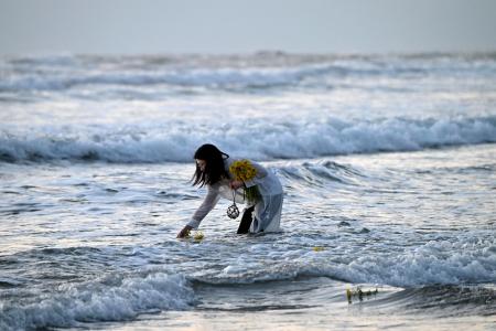 　東日本大震災で被災した福島県いわき市の薄磯海岸で、花を手向ける女性＝１１日午前５時４７分