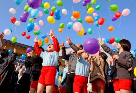 閉校する町野小で行われた記念イベントで、風船を飛ばす子どもたち＝２１日午後、石川県輪島市