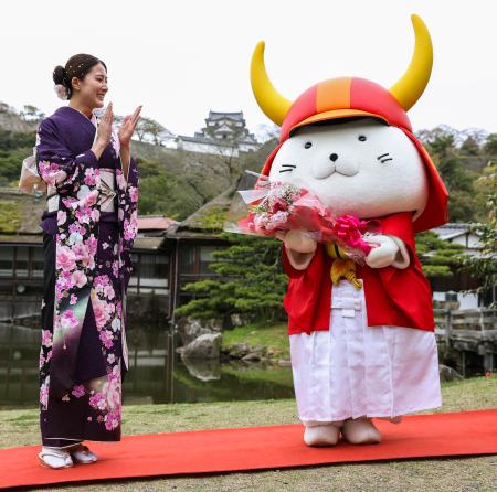 ２０回目の誕生日を祝う特別記念イベントで、大橋悠依さんから花束を受け取った「ひこにゃん」。奥は彦根城＝１３日午前、滋賀県彦根市