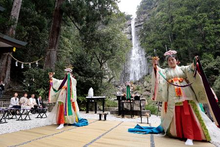 熊野那智大社の「桜花祭」で舞を披露する巫女。奥は那智の滝＝１４日午前、和歌山県那智勝浦町