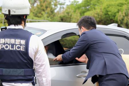 通行車両を呼び止め、情報提供を求めるチラシを配布する静岡県警の捜査員＝２１日午前、浜松市中央区