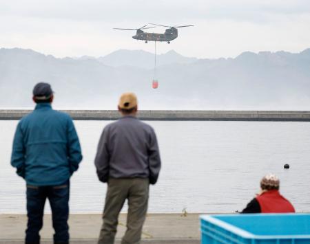 地元の漁業関係者が見守る中、山林火災の消火活動のため、海水をくみ上げるヘリコプター＝２８日午前、岩手県大槌町