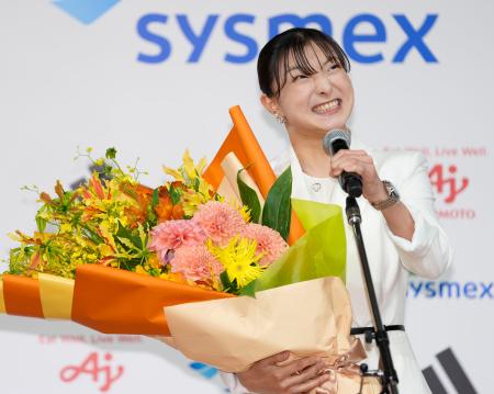 現役引退の記者会見で花束を手にマイクを握るフィギュアスケート女子の坂本花織=13日午前、神戸市内のホテル