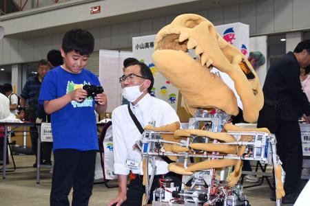 巡回型展示会「ＫＯＳＥＮ　ＰＡＲＫ」で、小山高専の名物ロボットを操作体験する来場者（左）＝１７日午後、宇都宮市