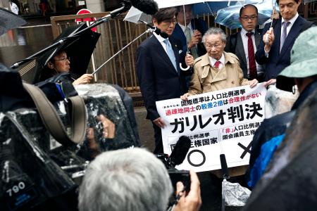 衆院選「１票の格差」訴訟の判決を受け、東京高裁前で「ガリレオ判決」などと書かれた紙を掲げる升永英俊弁護士（前列右から２人目）ら＝２１日午後