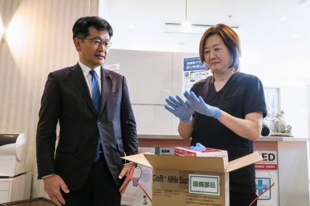 配送された国備蓄の医療用手袋を着ける「天王洲パークサイドビル歯科」の坂田香里院長。左は厚労省の仁木博文副大臣＝２３日午後、東京都品川区