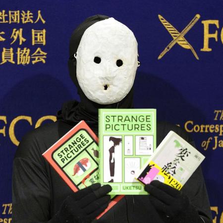 記者会見で著書を手にする覆面作家の雨穴さん＝２０２５年１月、東京都千代田区の日本外国特派員協会