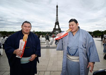 大相撲パリ公演を前に、エッフェル塔の前でフランスパンを食べる大の里（右）と豊昇龍の両横綱＝１１日、パリ（共同）