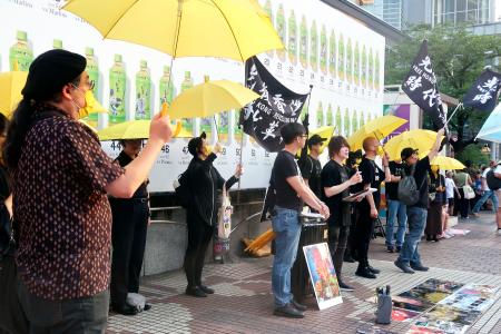 東京・渋谷駅前で開かれた在日香港人らの集会で、黄色い傘を掲げる参加者＝１３日午後