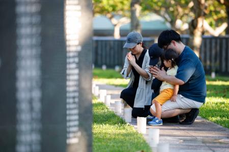 「慰霊の日」を前に、沖縄戦犠牲者の名前が刻まれた「平和の礎」に手を合わせる家族連れ=22日午後、沖縄県糸満市の平和祈念公園