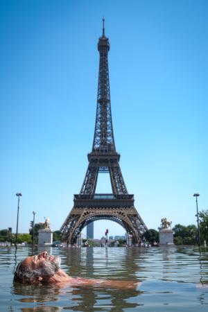 ２４日、パリのエッフェル塔前のトロカデロ庭園の噴水で涼む男性（ゲッティ＝共同）