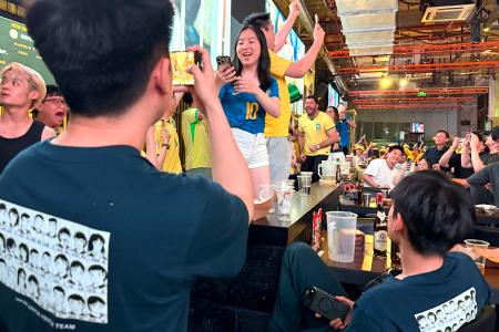 中国上海市のスポーツバーで、漫画「キャプテン翼」のイラストが描かれたＴシャツを着て、勝利を喜ぶブラジルファンを見つめる男性＝３０日（共同）