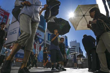 太陽が照りつける街中を、日がさを差して歩く人たち＝２０２５年９月、大阪市