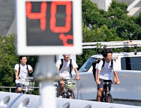 酷暑日となった愛知県豊田市で自転車に乗る人たち。街頭温度計は気温40度を示していた=23日午後