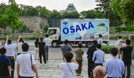 大阪府の職員らに見送られ出発する自走式トイレカー。奥は大阪城=29日午後、大阪市中央区