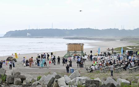 東日本大震災後初めてとなる１６年ぶりの海開きが行われた請戸海水浴場。奥には東京電力福島第１原発の排気筒が見える＝１日午前、福島県浪江町