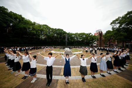 原爆落下中心地碑を囲む「高校生平和大使」らによる「人間の鎖」＝９日午前、長崎市の爆心地公園