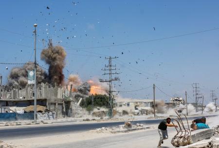 イスラエル軍の攻撃で、飛び散る破片から逃げる人たち=23日、パレスチナ自治区ガザ中部ザワイダ(ロイター=共同)